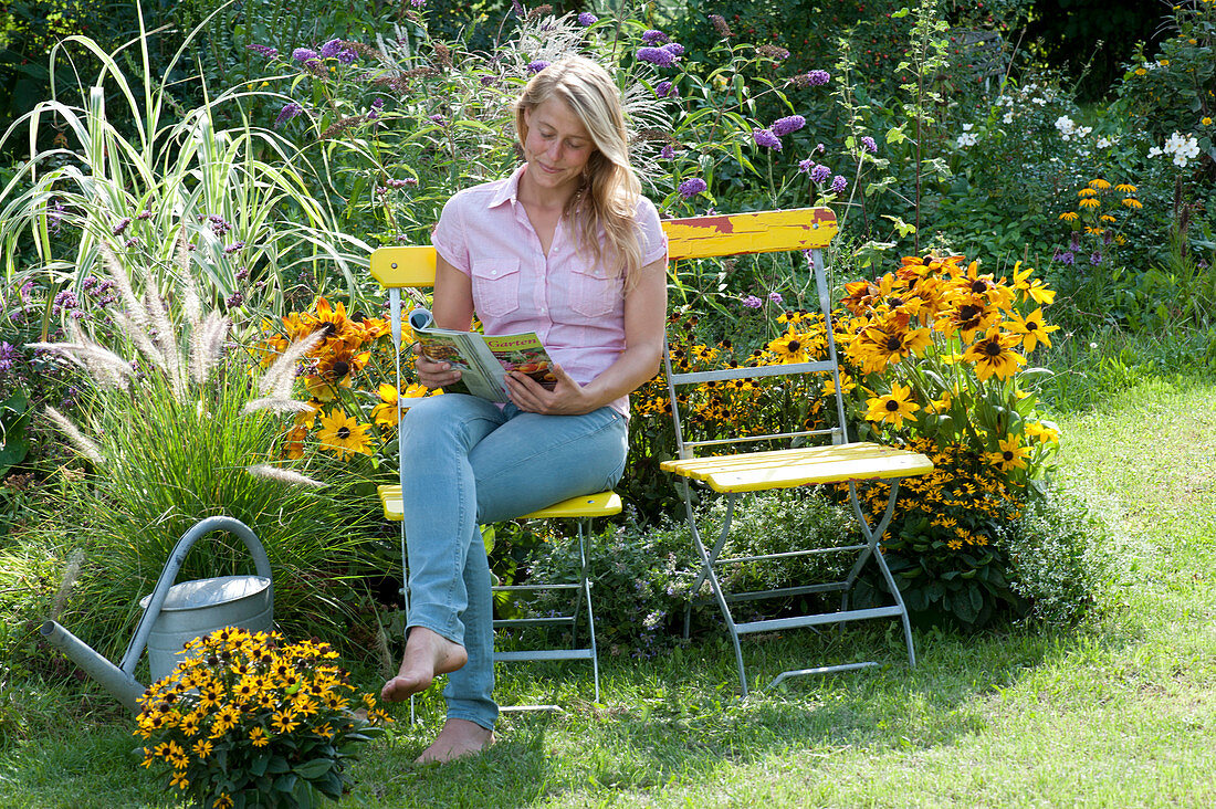 Woman sitting at the flower bed with Rudbeckia (Coneflower), Pennisetum 'Cassian'