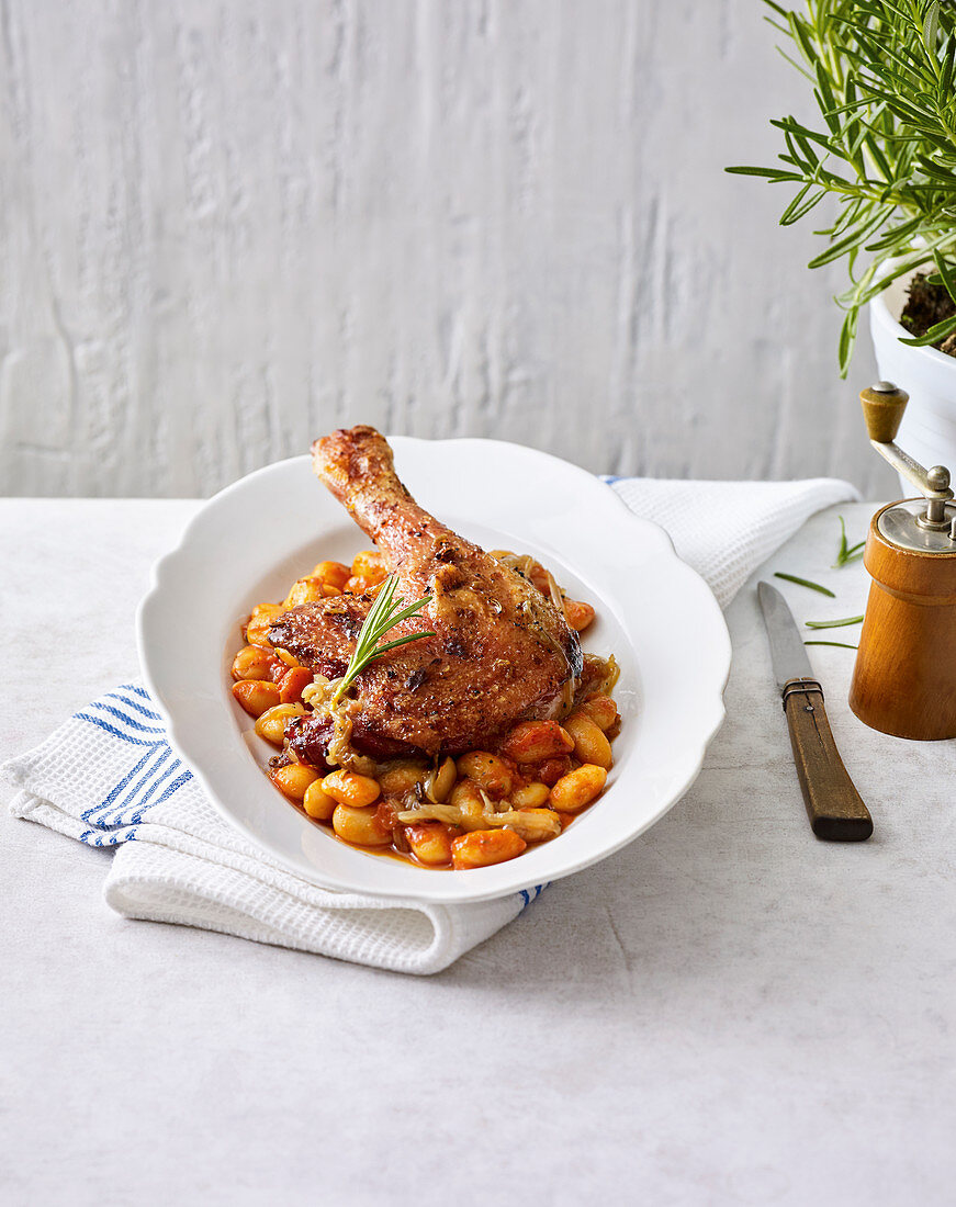 A cured duck leg with beans and tomatoes