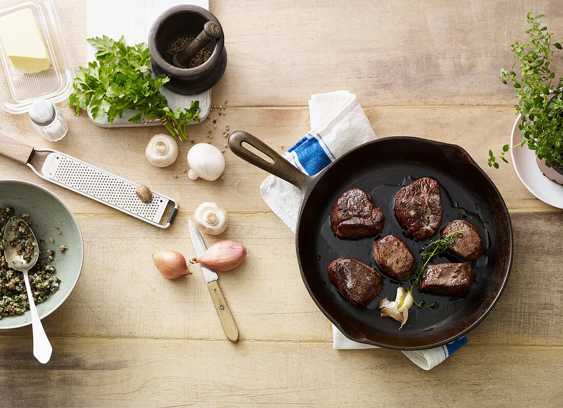 Venison medallions in a pan with the ingredients for a mushroom topping