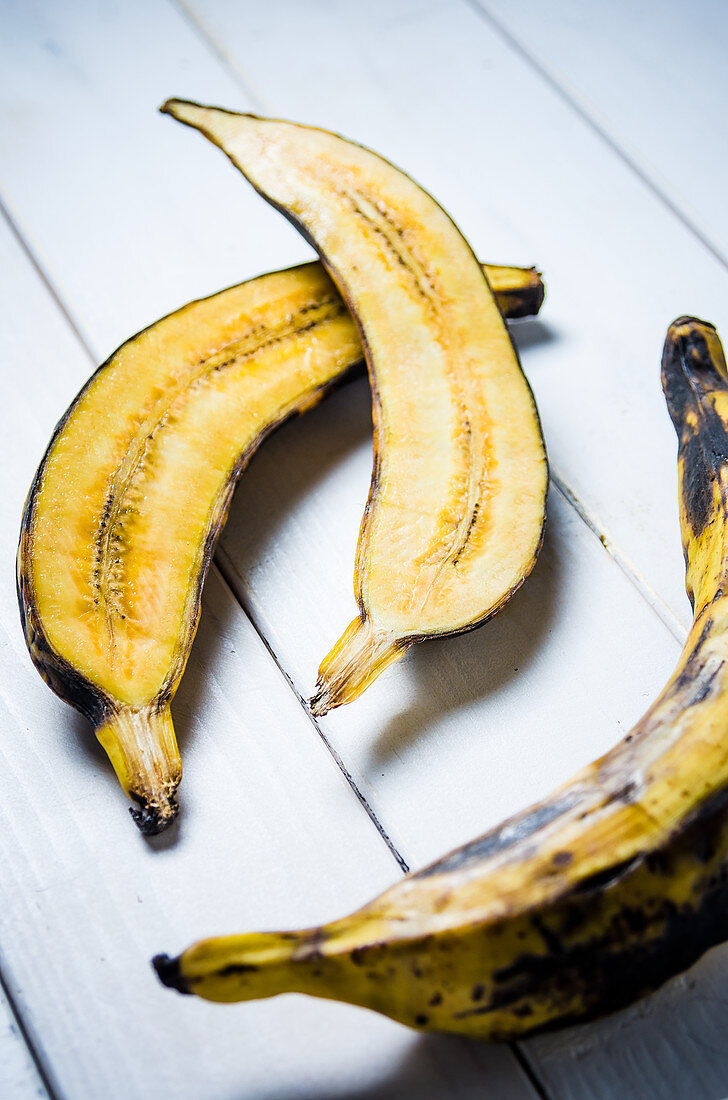 Plantain cut in half and whole on a white wooden background