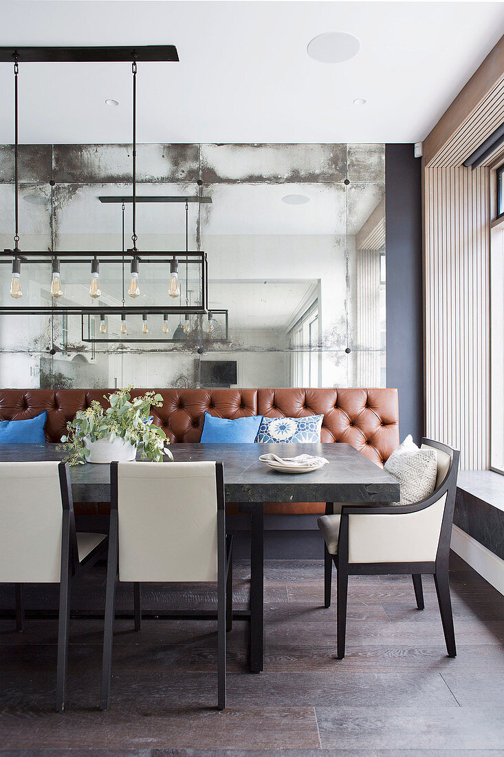 Dining table with natural stone top, upholstered chairs and leather bench against mirrored wall