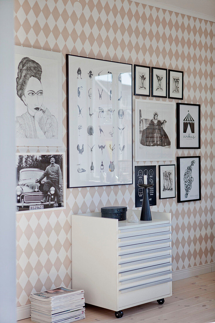 Plan chest on wheels below gallery of pictures on wall with diamond-patterned wallpaper