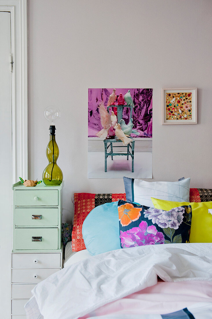 Patterned scatter cushions on bed with chest of drawers as bedside table