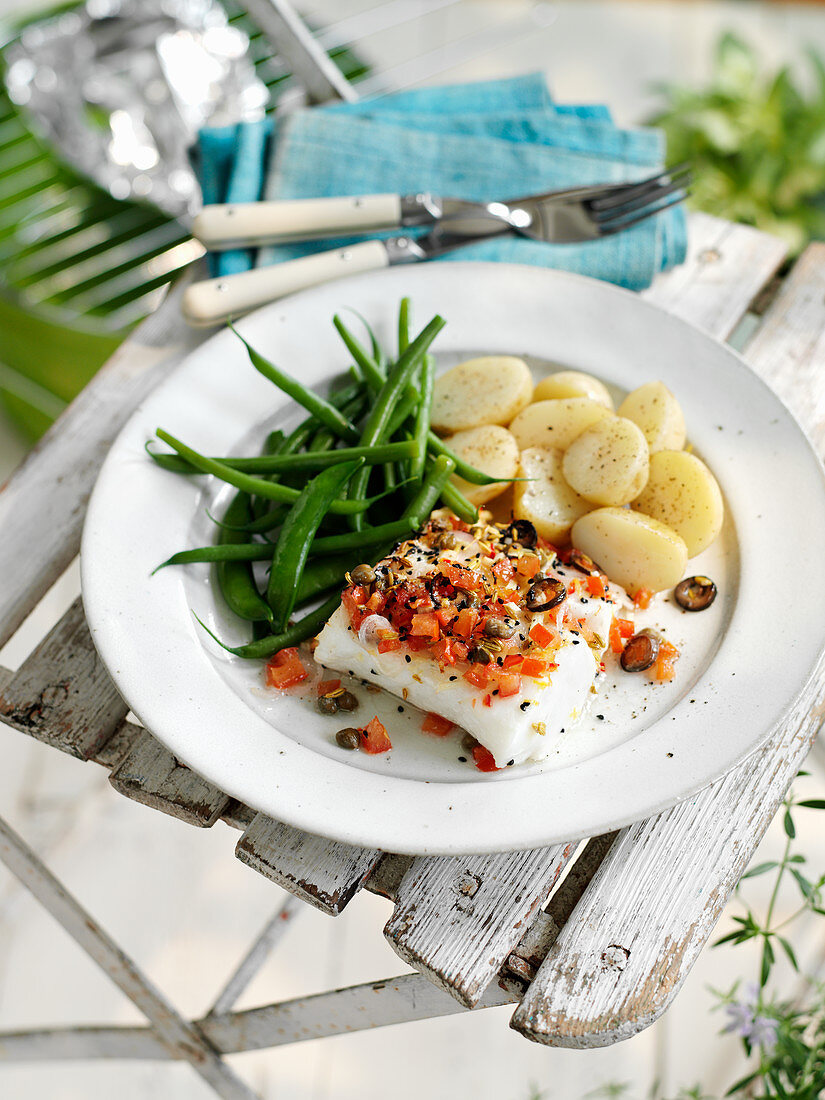 A cod fillet topped with vegetables and served with green beans and potatoes
