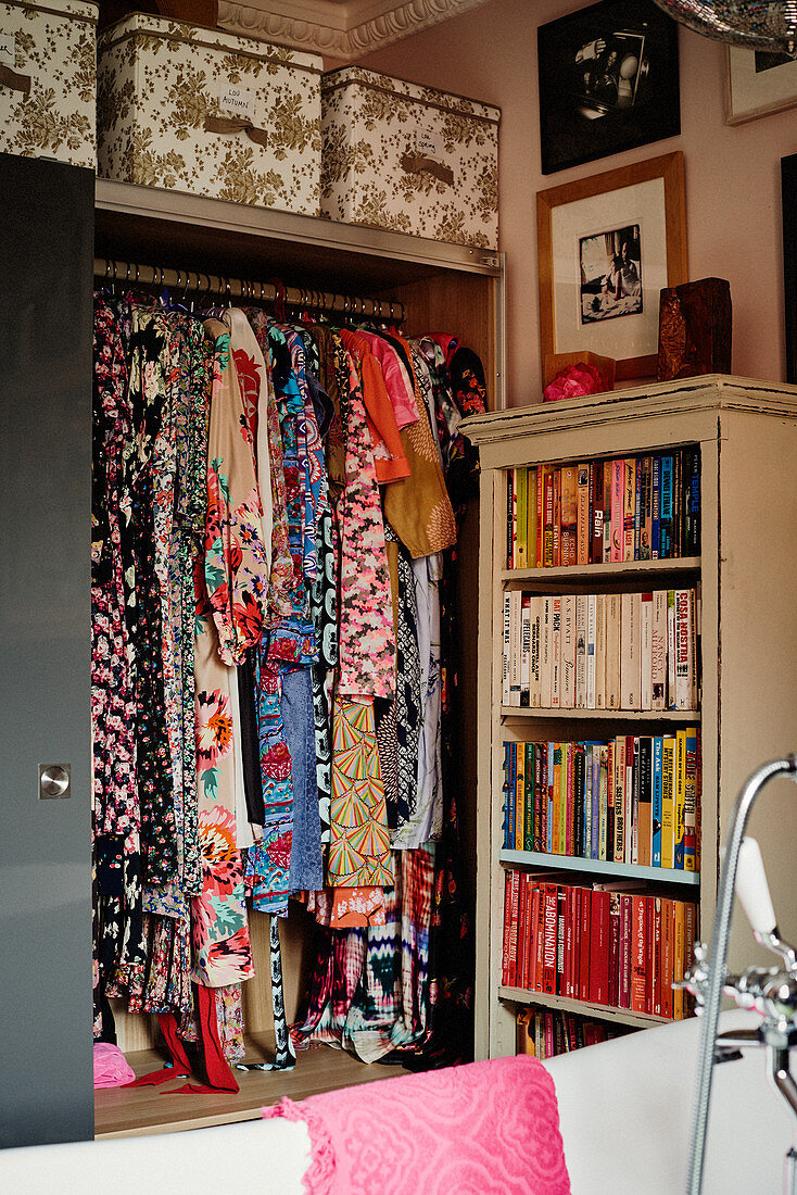 Colourful patterned dresses in open-fronted wardrobe and shelves of books sorted by colour