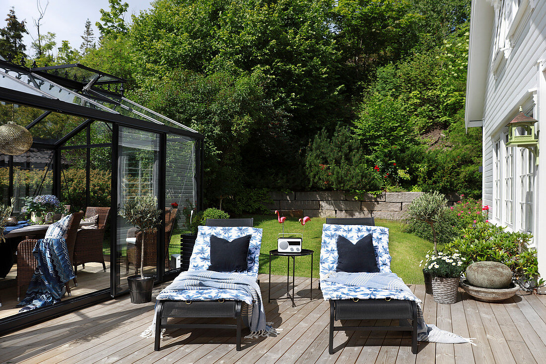 Two loungers on sunny wooden deck between conservatory and house