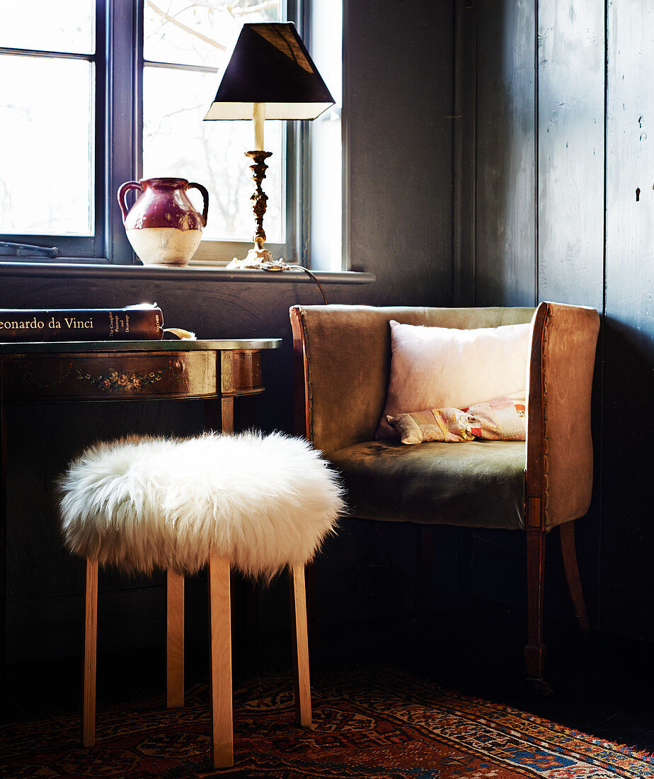 Stool with fur cover in front of old armchair below window