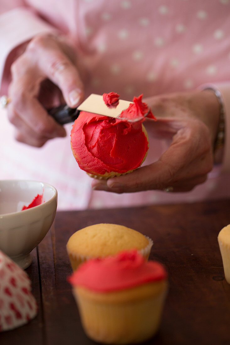 Cupcakes mit roter Glasur bestreichen