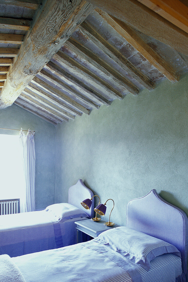 Twin beds with lilac headboards below wood-beamed ceiling