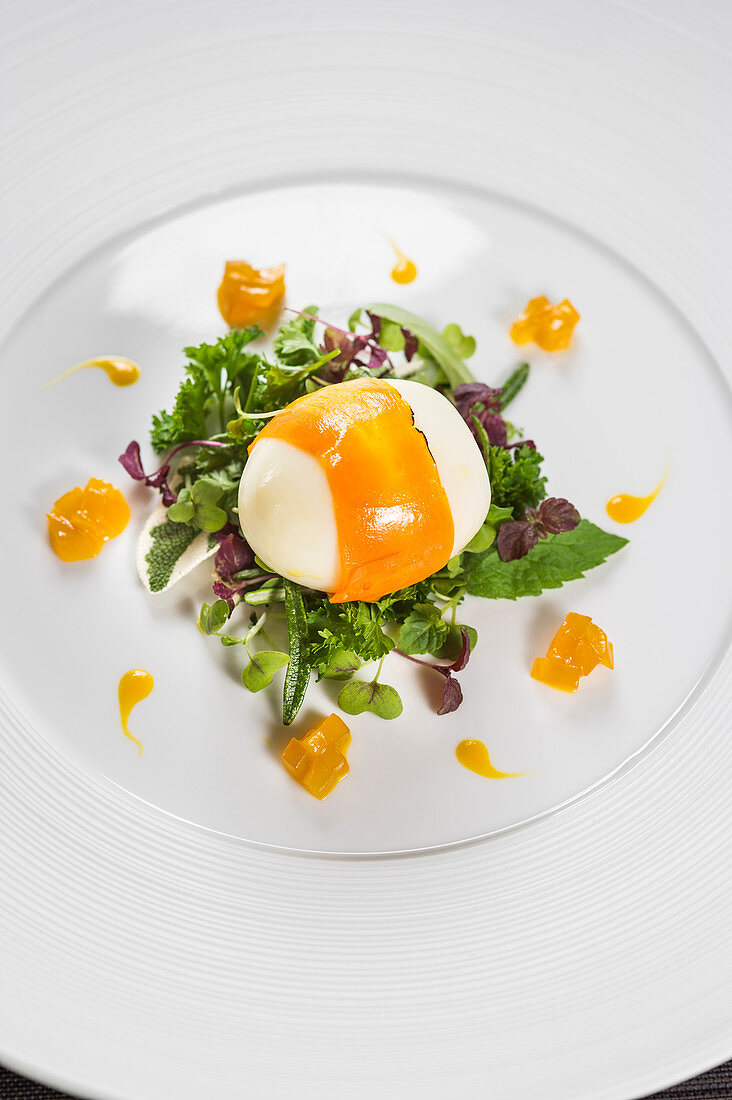 A poached egg wrapped in carrots with garden herbs and mango