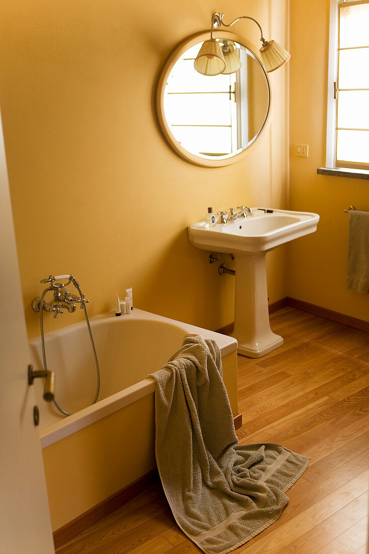 Bathtub and pedestal sink below round mirror in retro bathroom with painted walls