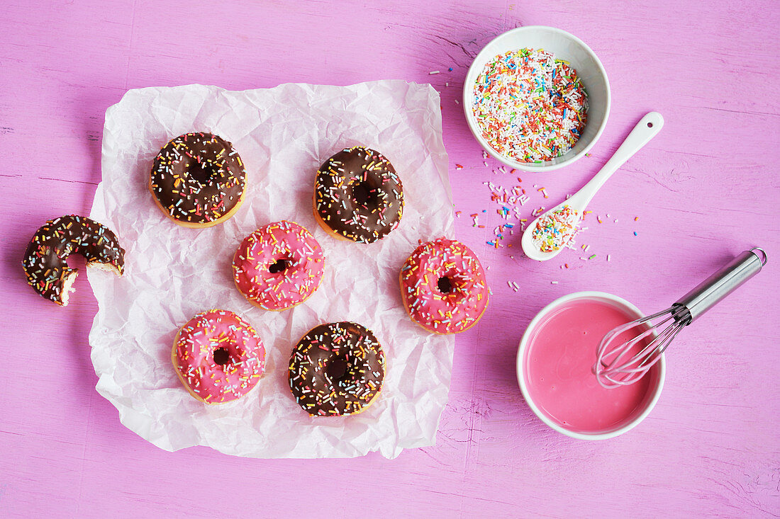 Mini-Donuts mit Schokolade, Zuckerglasur und Zuckerstreuseln auf Papier