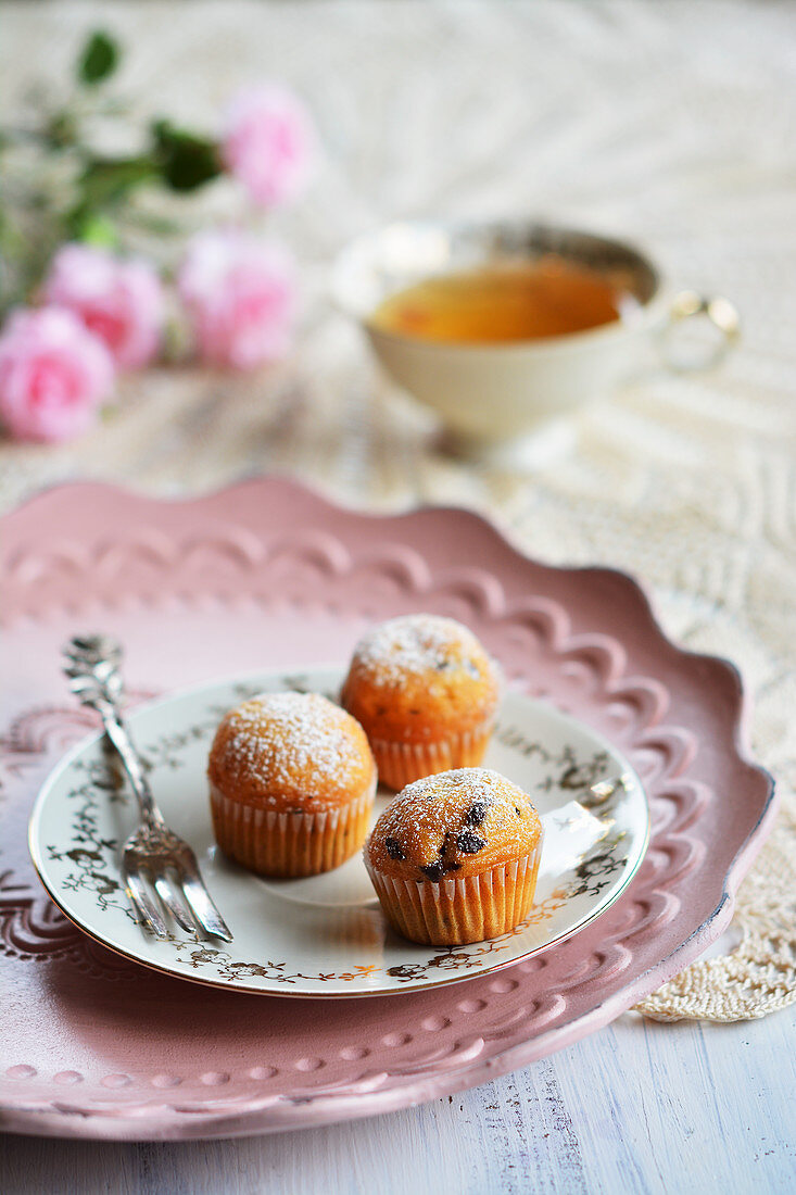 Kleine Muffins auf Teller mit Gabel, Teetasse und Blumen