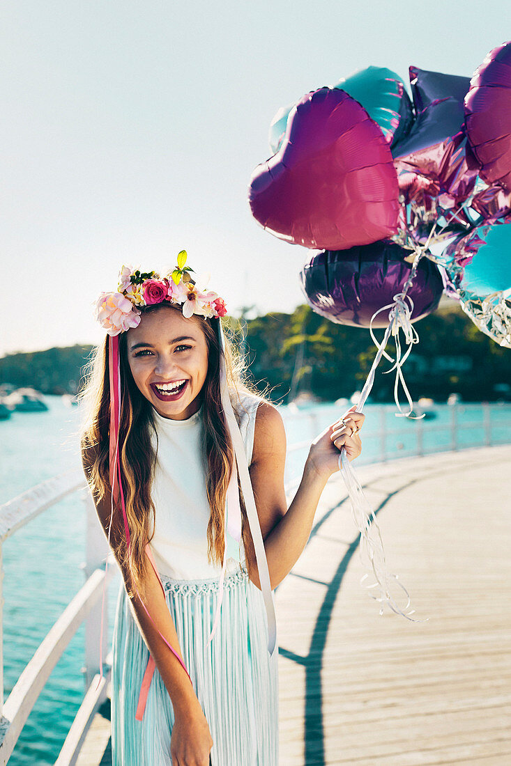 A girl holding a bunch of balloons wearing a wreath of flowers in her hair