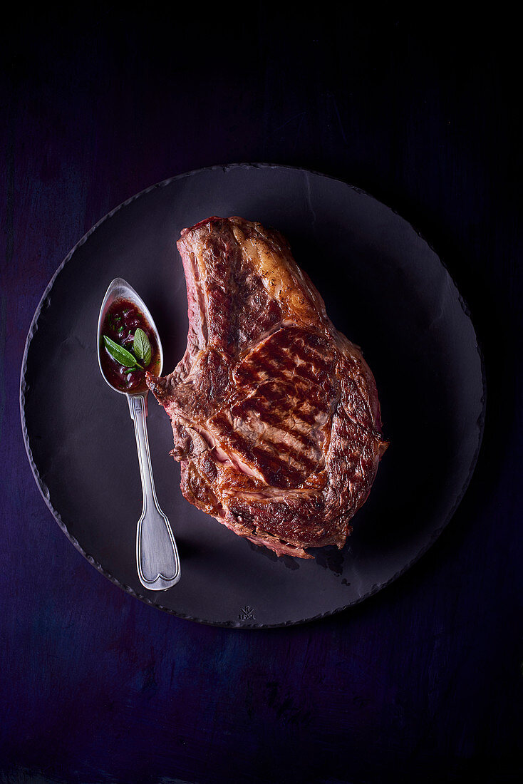 A beef chop on a black plate against a black background (top view)
