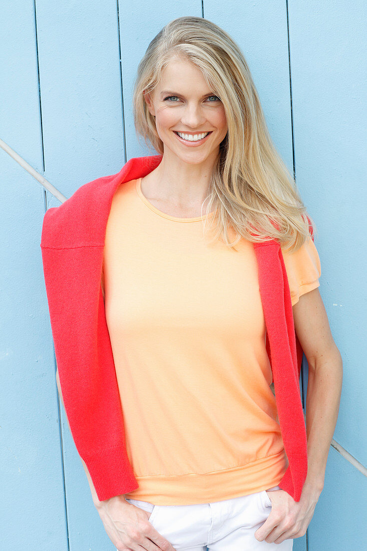 A young blonde woman wearing a yellow t-shirt with a red jumper over her shoulders