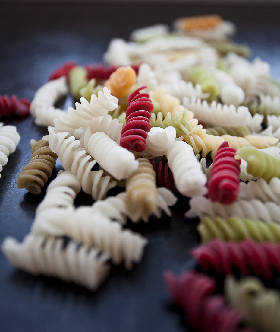 Colourful fusili pasta made from vegetables (beet, spinach), on a black countertop