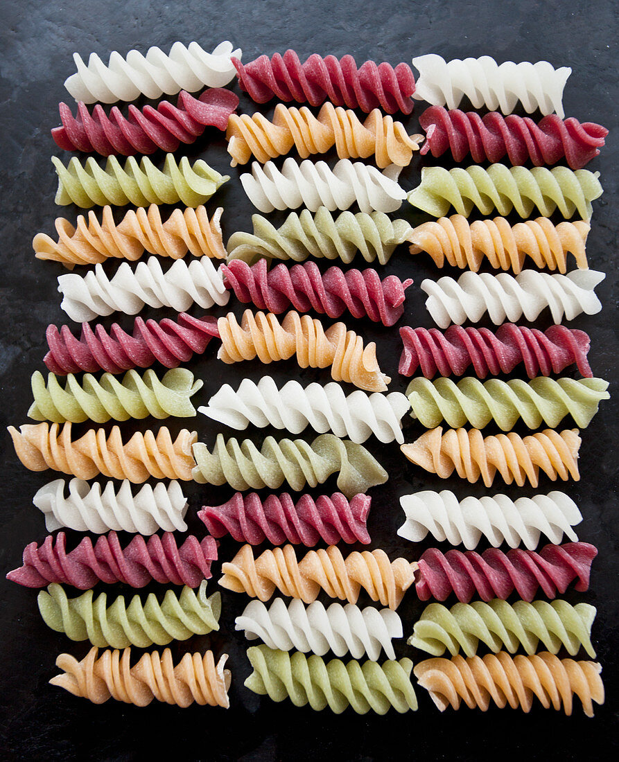 Colourful fusili pasta made from vegetables (beet, spinach), on a black countertop