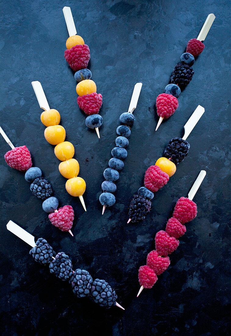 Frozen berries on wooden skewers - blackberries, raspberries, blueberries and golden berries