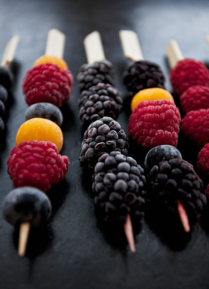 Frozen berries on wooden skewers - blackberries, raspberries, blueberries and golden berries