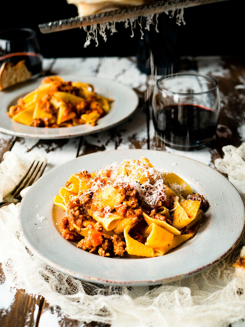 Pappardelle bolognese on rustic table grating cheese
