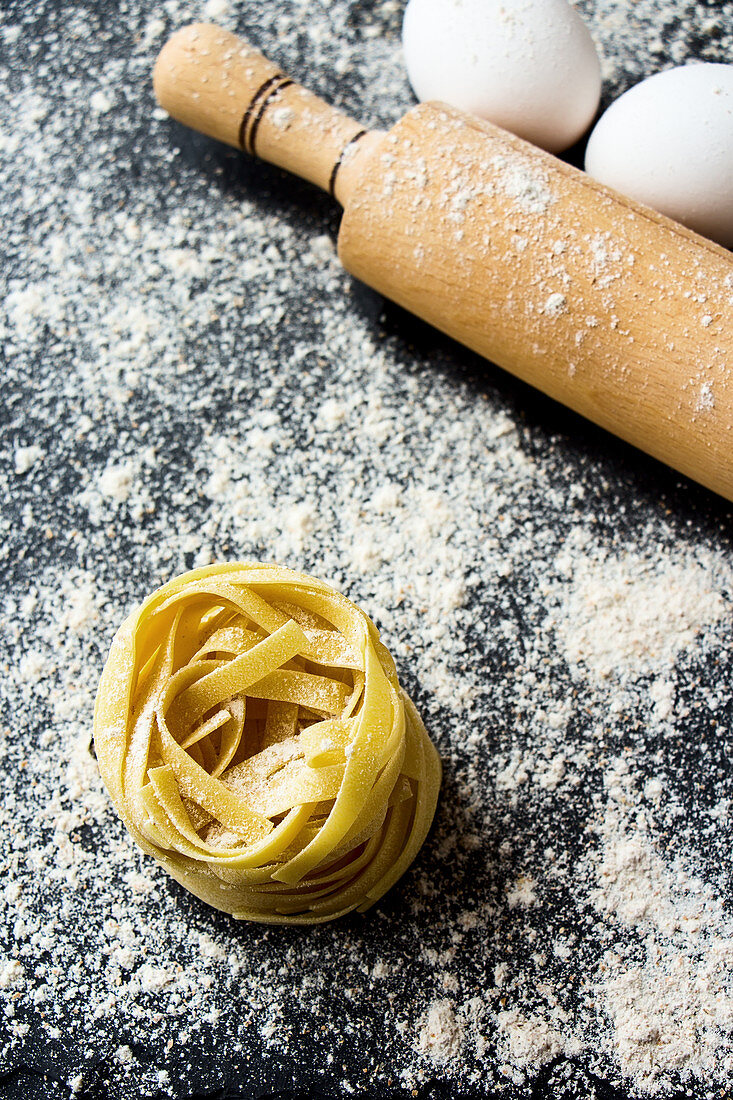 Ribbon pasta with a rolling pin on a floured work surface (top view)