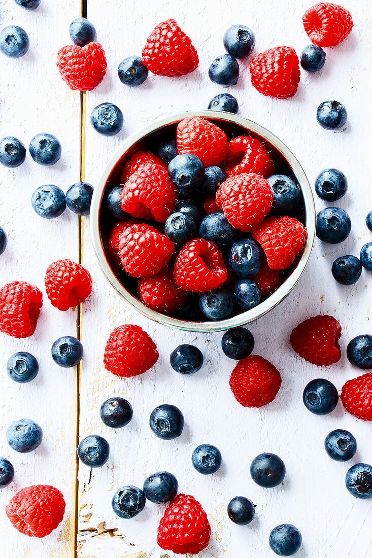 Himbeeren und Blaubeeren in Schälchen und auf Holzuntergrund (Aufsicht)