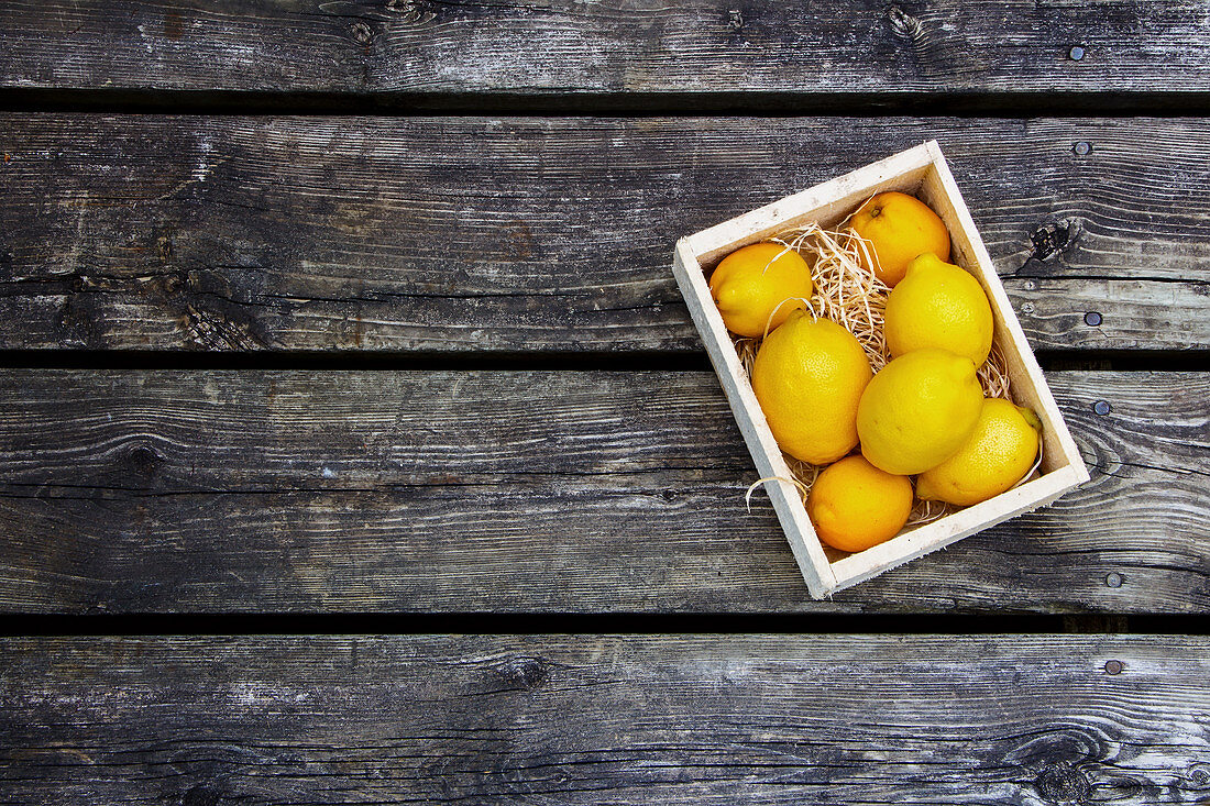 Zitronen in Holzkiste auf Holzuntergrund (Aufsicht)