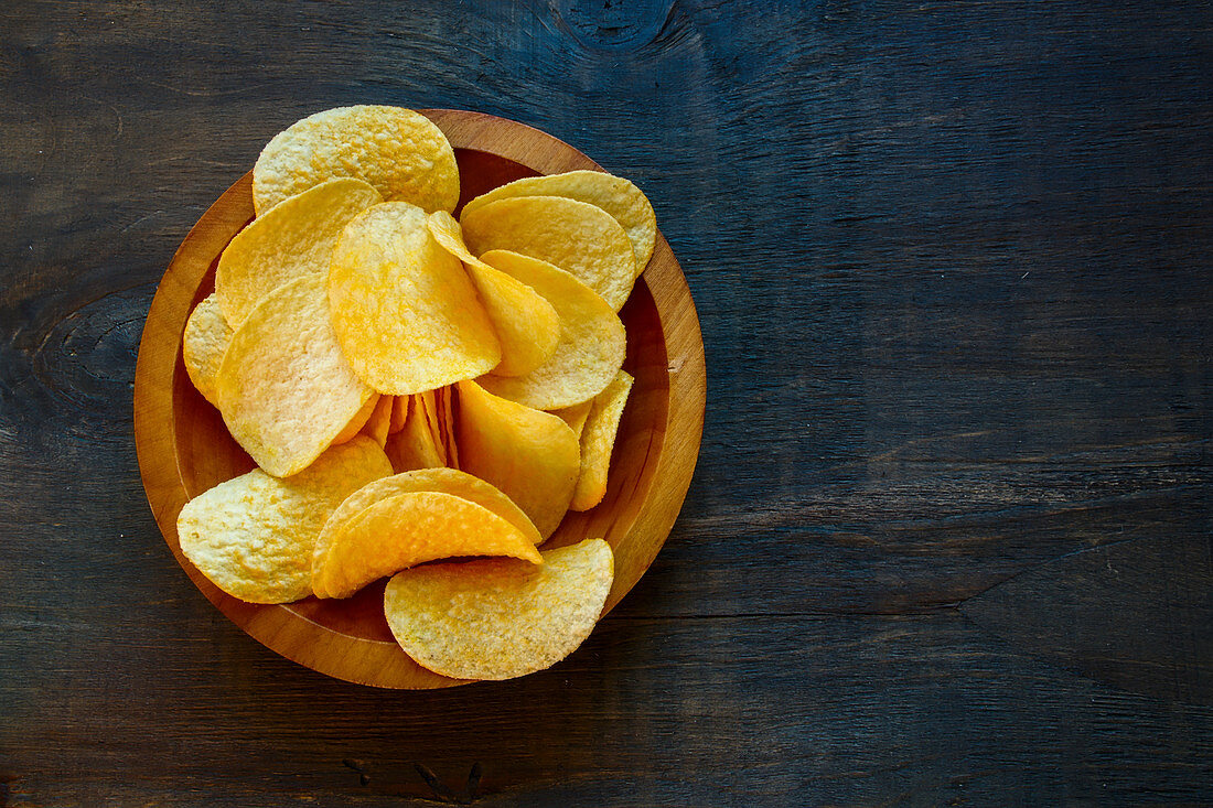 Crisps in a wooden bowl on a dark wooden surface (seen from above)