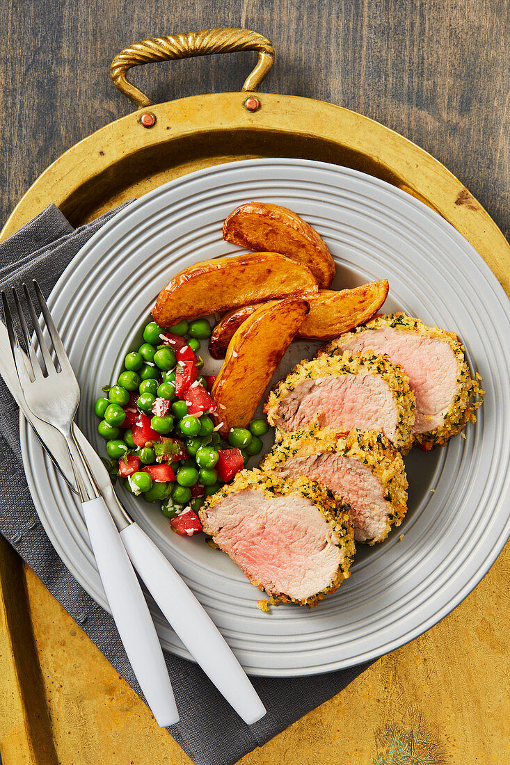 Herb-crusted pork tenderloin served wtih potato wedges and peas and tomatoes