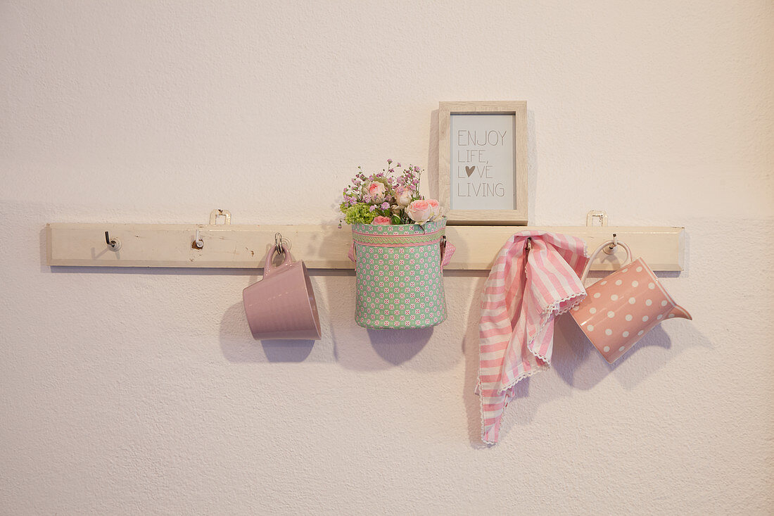 Stoffkörbchen mit Blumen und Geschirr an einer Hakenleiste