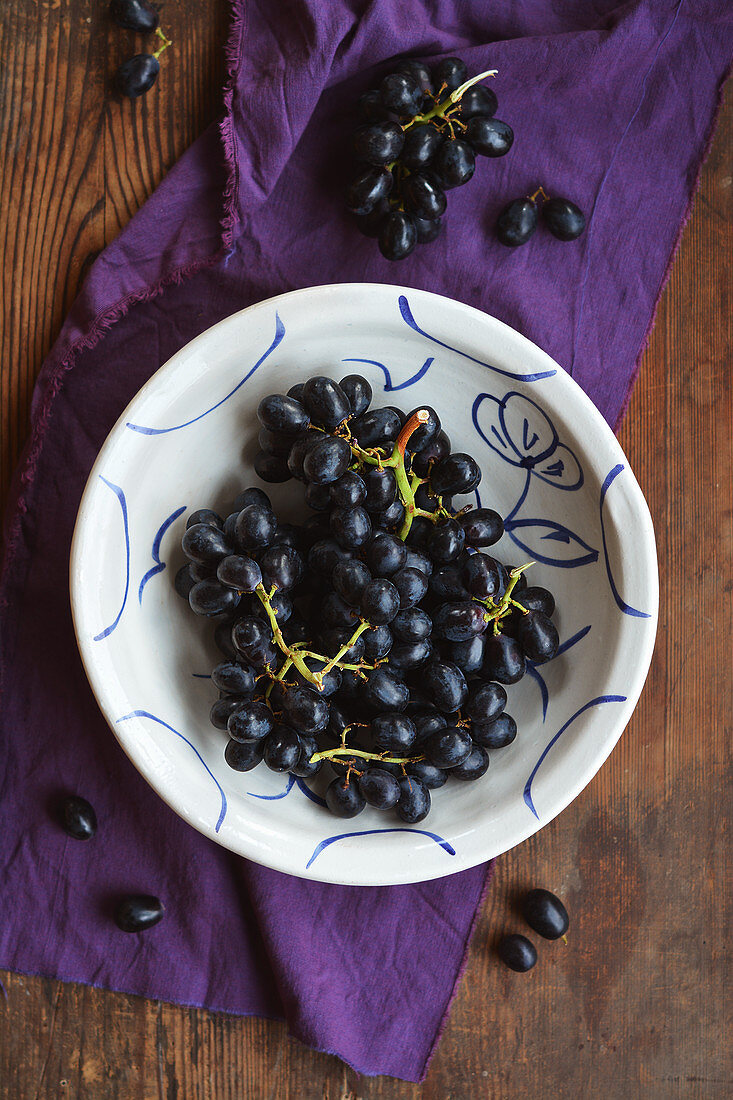 Blaue Weintrauben in rustikaler handbemalter Schale auf Holztisch