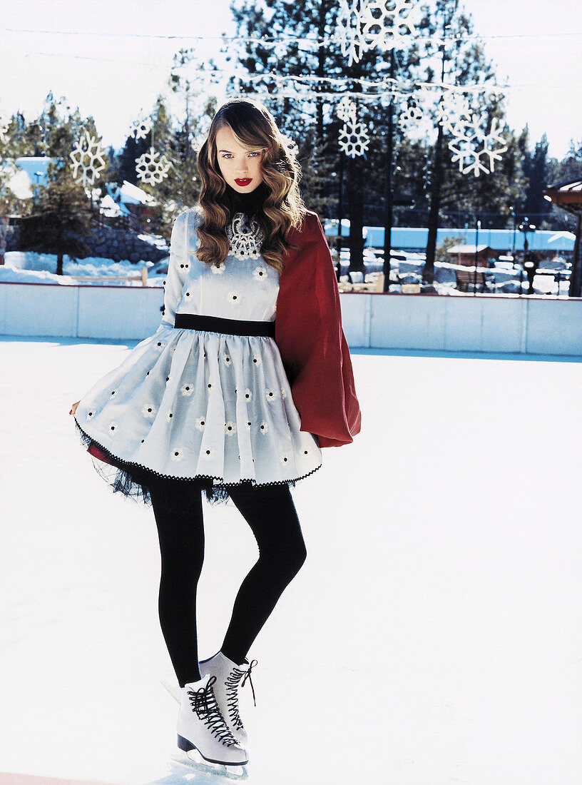 A young woman wearing an elegant retro dress, black tights and skates on an ice rink