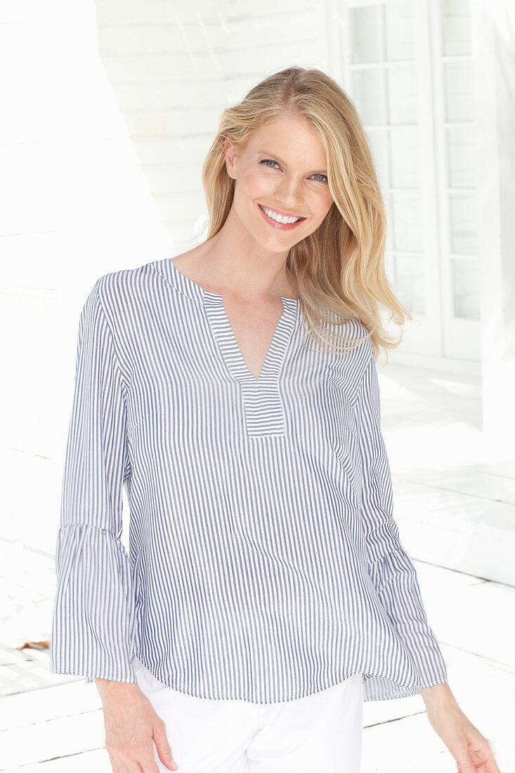 A young blonde woman on a terrace wearing a striped blouse and shorts