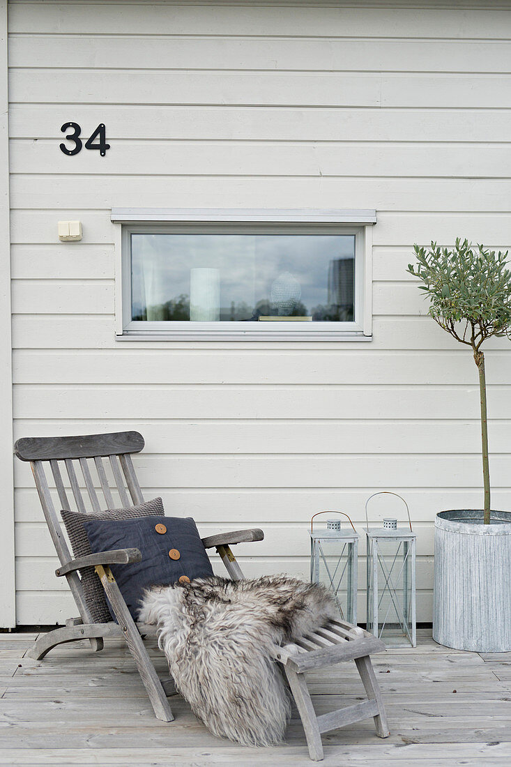 Cushions and fur blanket on lounger outside house with house number on wall