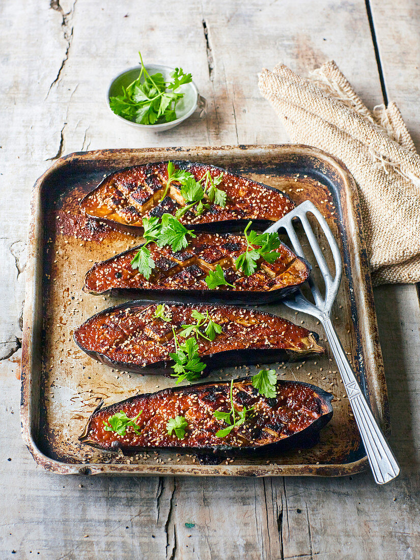 Glazed miso aubergines on a baking sheet with sesame and cilantro
