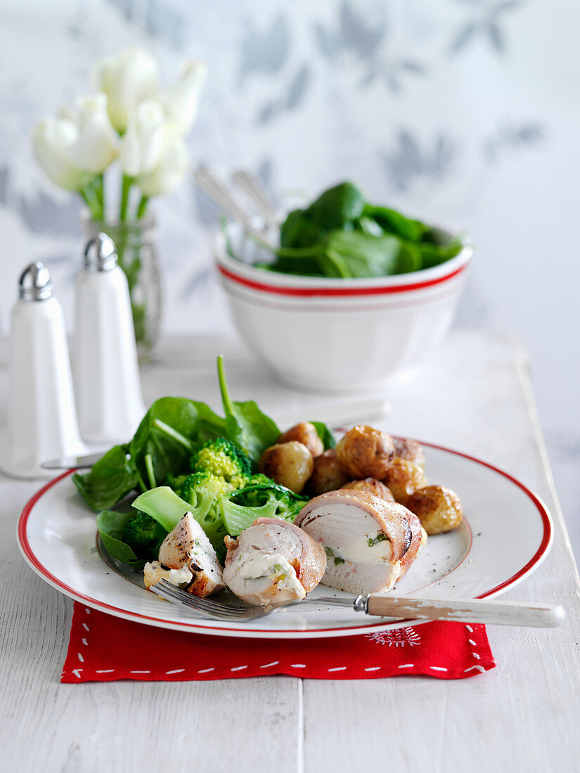 A chicken breast wrapped in bacon with potatoes and broccoli