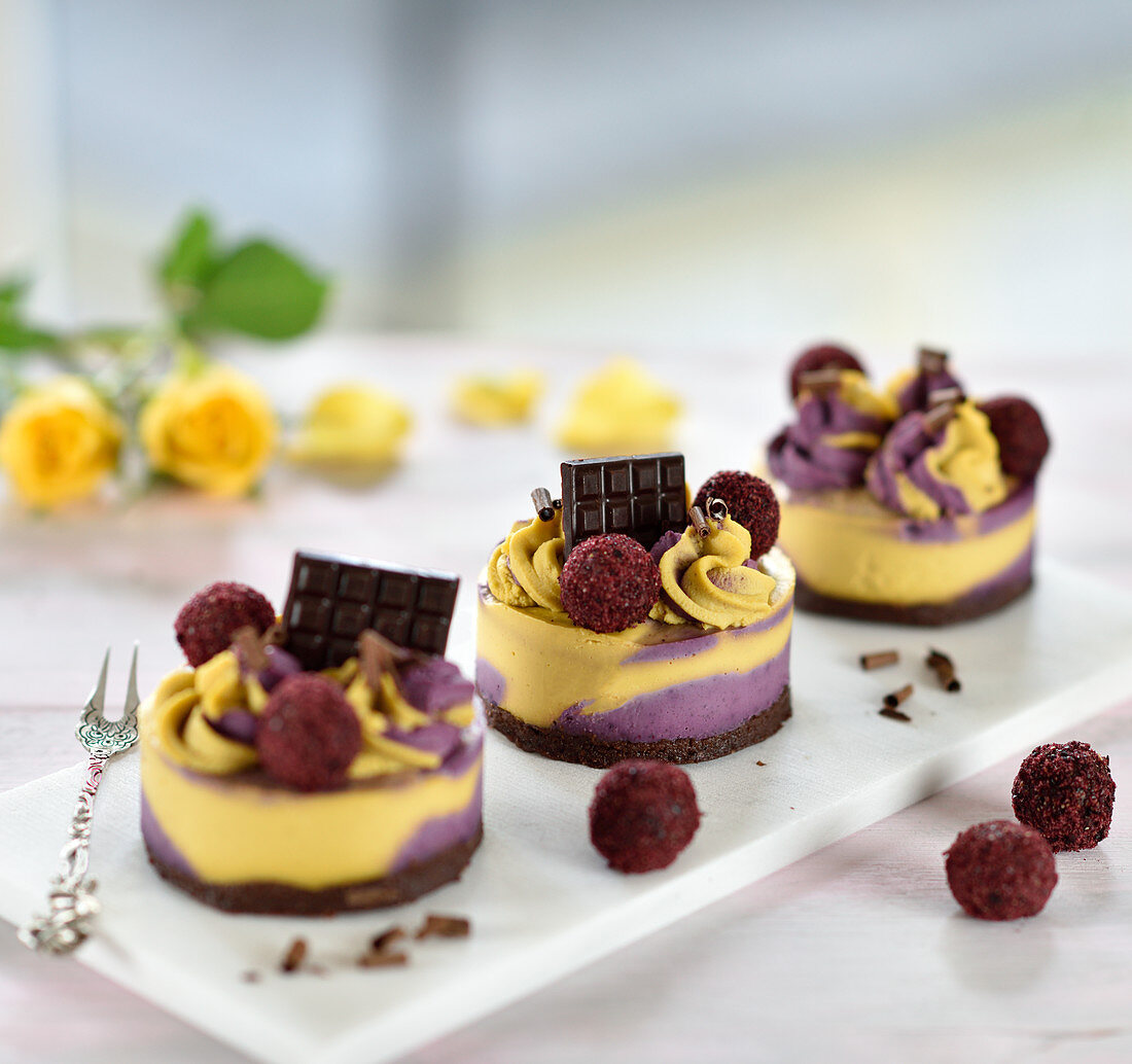 Rohvegane Cassis-Mango-Törtchen mit Schoko-Mandelboden, dekoriert mit fruchtigen Schokokugeln und Schokolade