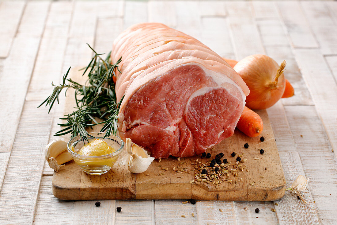 Pork roasting joint with ingredients on a chopping board