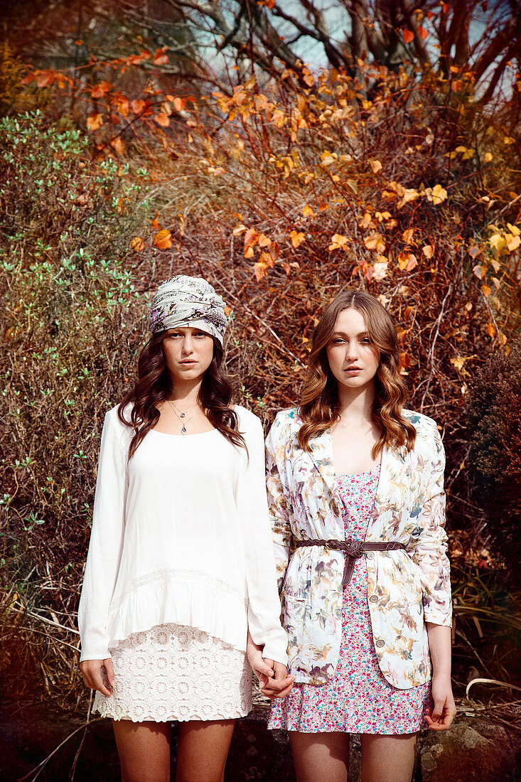 Two young women standing in front of an autumnal bush