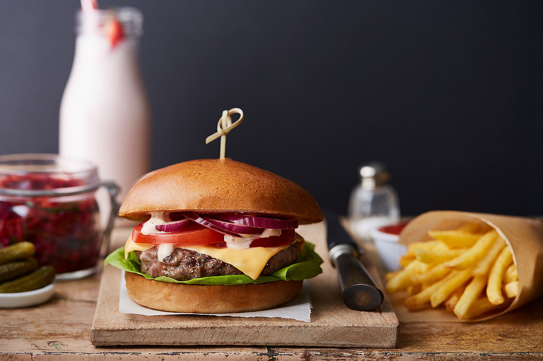 A beefburger with chips on a wooden chopping board