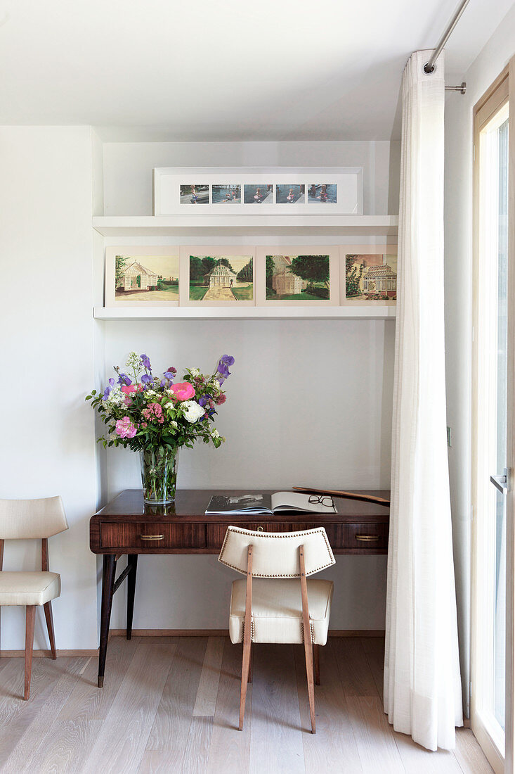 Upholstered chair at antique desk with vase of flowers in niche