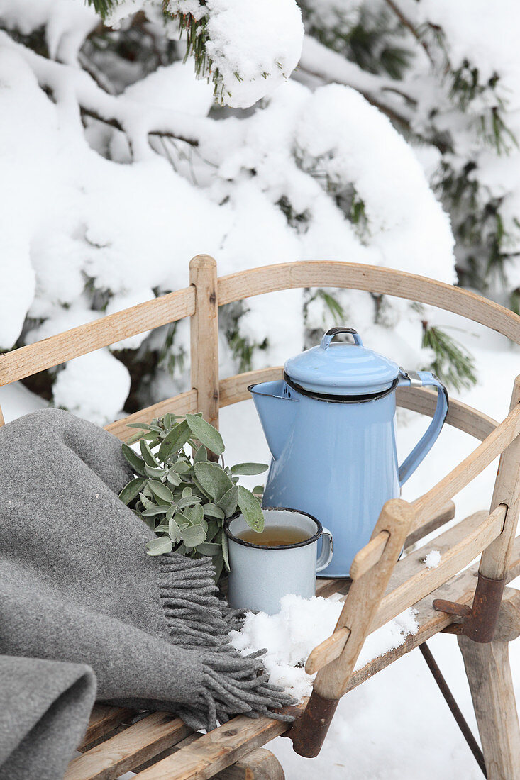 Blechkanne und Teetasse auf Holzschlitten im Schnee