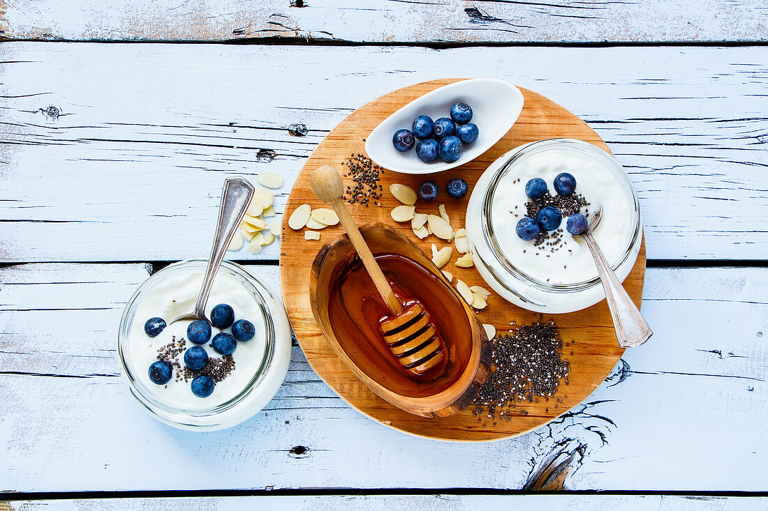 Mason jars of breakfast yogurt with chia seeds, honey and fresh blueberries on white grunge wooden background