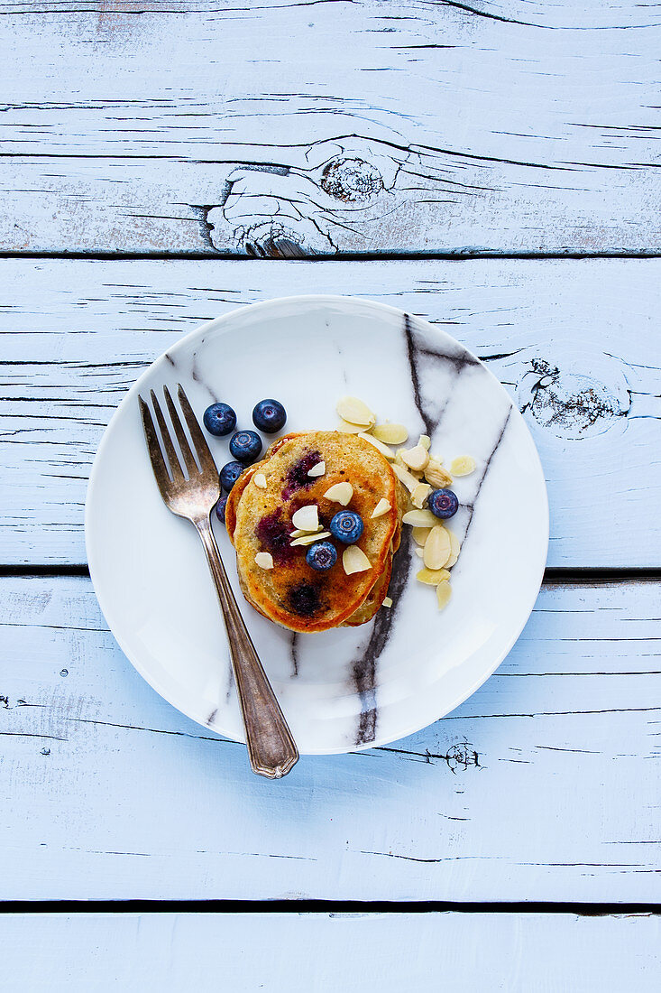 Plate of delicious blueberries homemade pancakes with honey and almonds for breakfast on rustic wooden white plywood background