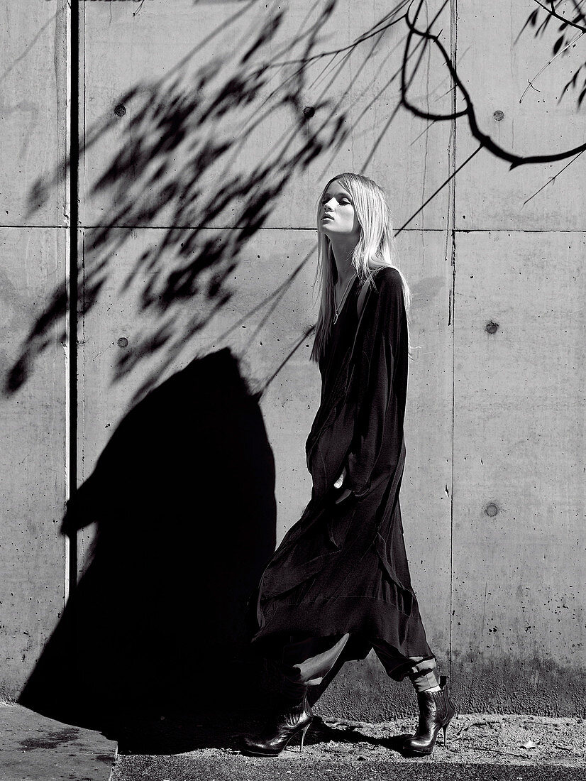 Junge Frau in schwarzem Longcardigan vor Betonwand (s-w-Aufnahme)