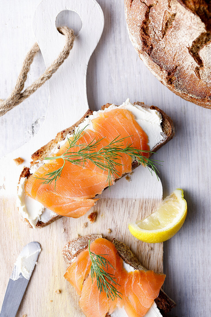Two slices of bread with cream cheese, salmon and dill on a wooden board