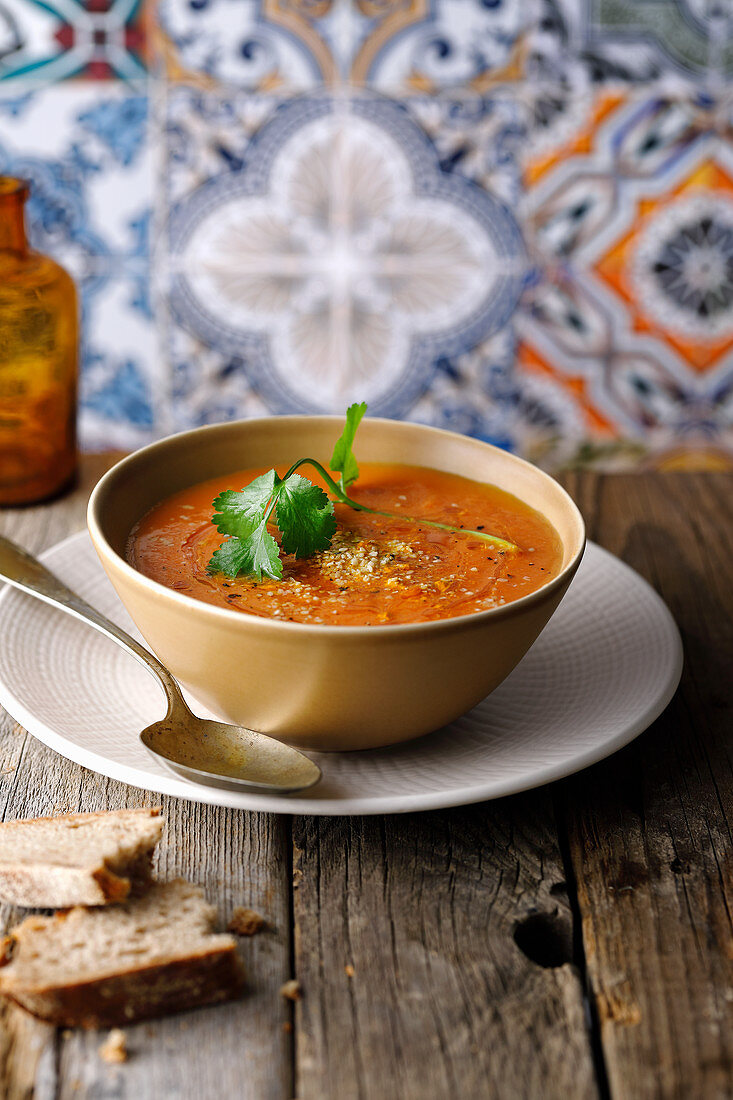 Spicy carrot soup with coriander and bread in an oriental setting