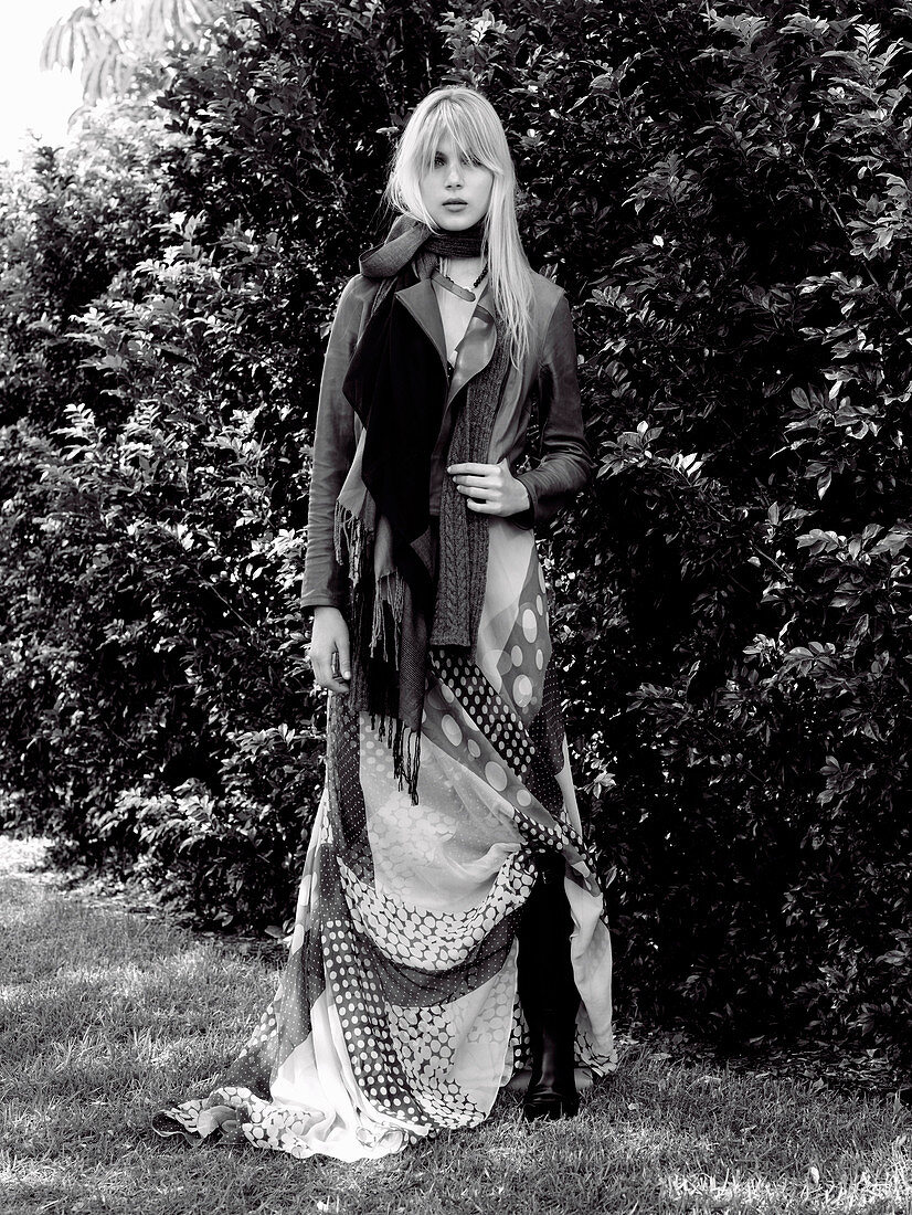 A young blonde woman in a park wearing a printed dress and a jacket (black-and-white shot)