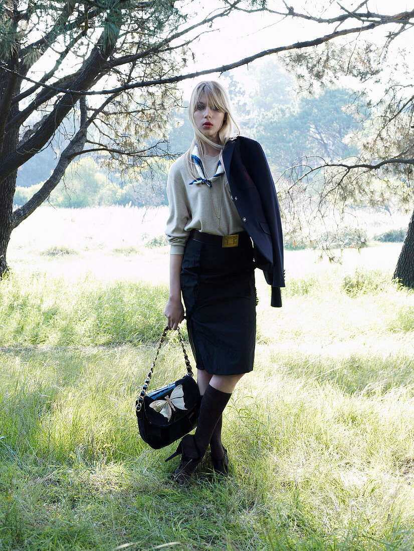 A young blonde woman standing under a tree wearing a business outfit